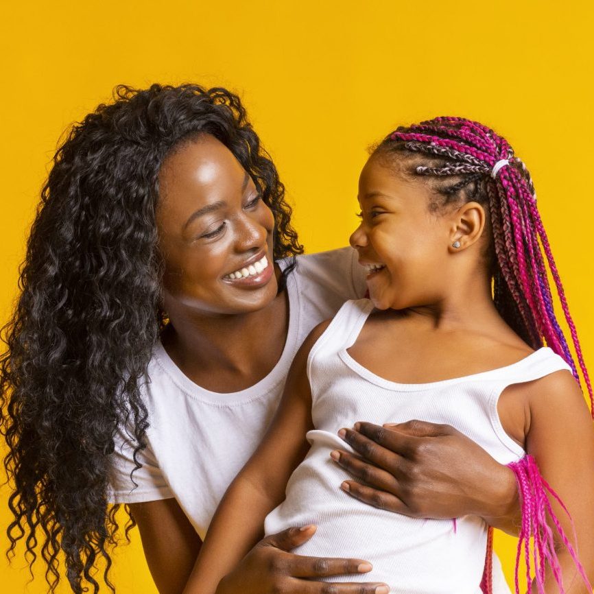Mother and daughter connection. Happy afro woman cuddling little girl, looking to her child with love and care.