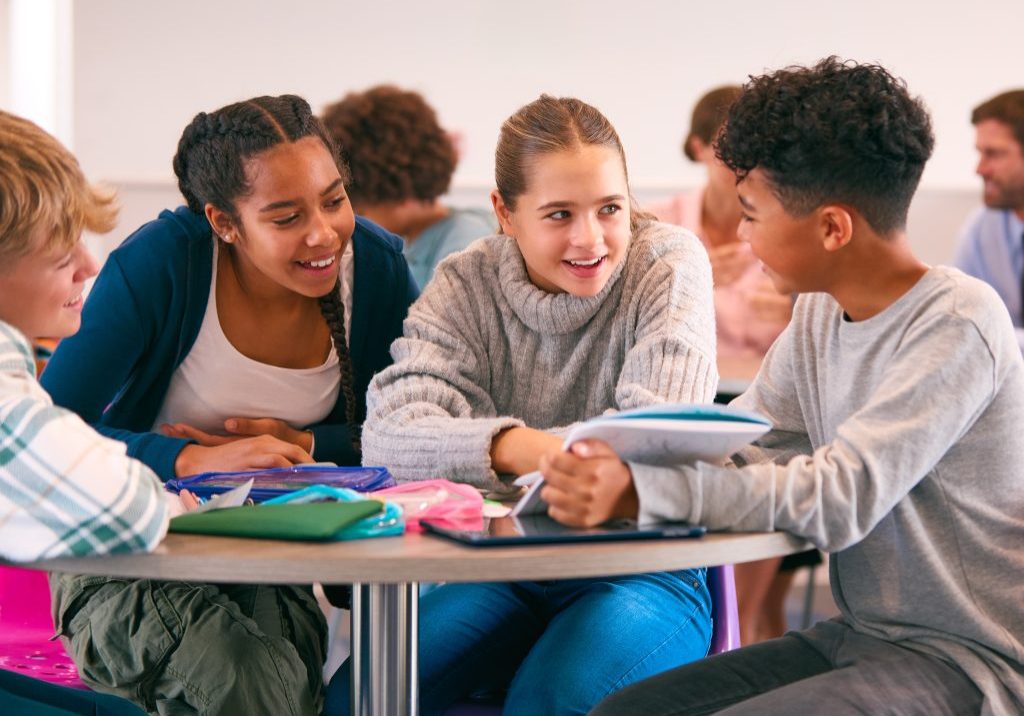 Secondary Or High School Students Collaborating In Study Area With Teachers In Background